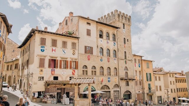 Shops, cafés, and medieval buildings with heraldic flags on Piazza Grande in Arezzo, Italy.