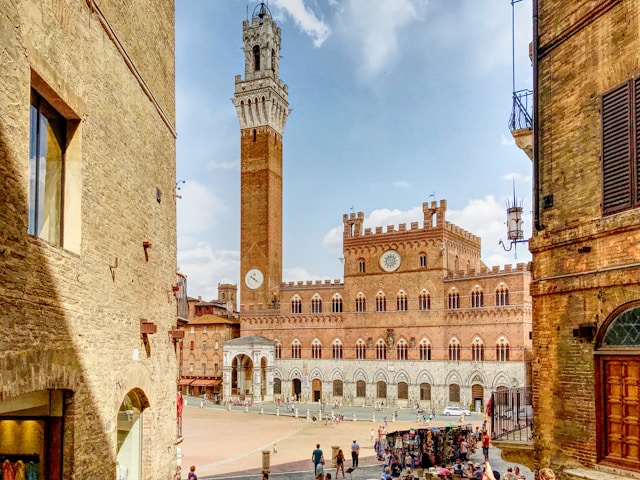 Palazzo Pubblico and Torre del Mangia in Siena's Piazza del Campo, with people gathered below.