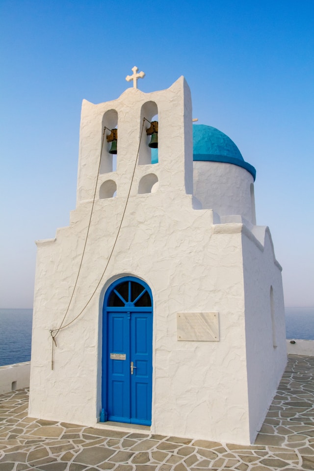 Small white chapel with a blue dome and bell tower in Greece. 